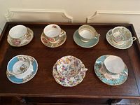 Overhead view of 7 teacup and saucer pairs arranged in two rows on wooden surface