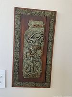 Full front view of the carved stone wall art mounted on wood showing intricate patterns and figure detail.