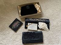 Four assorted hand purses arranged on carpet. One black beaded clutch in a box, one with floral bead detailing, one with floral embroidery, and one embellished with silver beads along the edges.