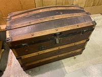Full view of dome top antique iron bound steamer trunk showing wooden slats, metal rivets, and curved top structure.