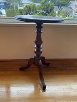 Side view of antique round table showing pedestal base with three legs and round top.