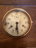 Front view of antique ships clock showing white face, black numerals, and 24-hour subdial.