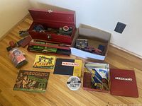 Overview of Meccano collection showing metal toolbox, boxes with parts, and instruction manuals.