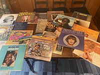 Photo shows 20 assorted vinyl records laid out on a wooden table. Album covers visible include Johnny Cash, Nat King Cole Ramblin Rose, Dusty Springfield, Dee Dee Sharp, and some disco and soul records.