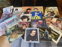 Top-down view of twenty vinyl record albums spread on a wooden surface, featuring a variety of artist and album covers including Elvis, Patsy Cline, Ray Conniff, and others.