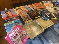 Photo of the 20 vinyl record album covers spread out on a table showing various artists and some wear on covers.