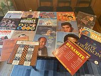 Photo showing 15 vinyl record covers laid out on a table including various artists and solo albums in used condition.