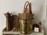 Photo showing various items including large metal ice bucket, wicker baskets on top, copper pitcher, small wooden barometer, round metal tray, and two clocks.