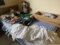 Vintage dolls, assorted stuffed animals including a panda, and white ruffled linens spread out on bed and box.