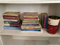 Books and two vintage tins on a white shelf.