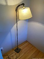 Full view of one vintage floor lamp showing twisted metal pole and cream fabric lampshade with scalloped edges.