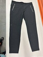 Full view of the dark gray sweat pants laid flat showing zippered pockets and tapered legs.