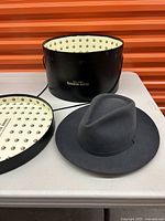 Goorin Bros dark gray felt fedora hat displayed with original black round hat box with gold branding and patterned interior.