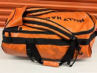 Side view of the Helly Hansen orange waterproof duffel bag showing padded shoulder straps and carry handles.