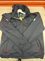 Front view of black waterproof Helly Hansen jacket with red zipper pulls shown on white hanger.