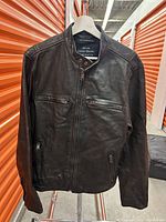 Front view of dark brown leather jacket with zipper and pockets.