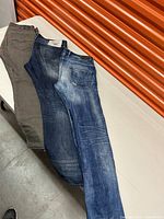 Three pairs of men's jeans laid side by side showing varying washes and colors: grey, medium-dark blue, and light blue with distressing.