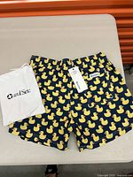 Men's swimming shorts displaying full pattern and waistband, with attached tags and branded pouch included.