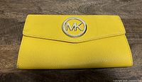 Front of yellow pebbled leather Michael Kors clutch with MK logo.