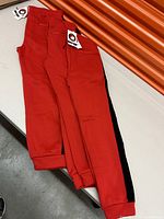 Two pairs of red sweatpants laid on a table, showing the front side with pockets and elastic waistbands with drawstrings.