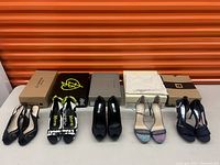 Five pairs of female high heels displayed on table with shoeboxes behind them, showing variety of colors and styles.