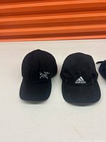 Two black hats on display, one with a white unknown logo and the other with an Adidas logo.
