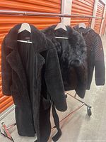Three women's jackets on a rack: a Carbone black fur coat, a black fur vest, and a Michael Kors black quilted jacket.