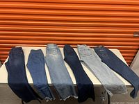 Seven pairs of women's jeans laid out, various shades of blue denim from dark to light wash, showing styles and condition.