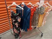 Photo of six women's summer dresses on hangers on a metal rack, showing styles and colors.