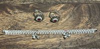 Two adjustable silver toe rings with red stones and clear stone accents, and silver ankle bracelet with clear stones and dangling bells laid on wooden surface