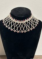 Front view of the silver Indian necklace displayed on a black bust, showing the full lattice pattern and the red and clear stones along the edges.