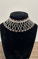 Front view of the silver lattice necklace on a black display stand showing overall design and stone placement.