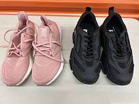 Pair of pink adidas training shoes with knit mesh upper and white cushioned sole next to black Steve Madden sneakers with chunky sole and mesh overlays.