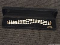 Photo showing full length of three-strand pearl-like stone bracelet with 14k gold clasps in a black jewelry box.