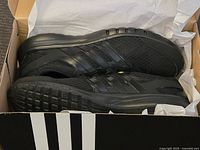 Side and sole view of the brand new Adidas black sneakers inside the box