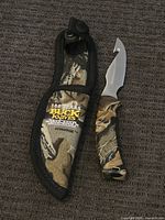Display of knife and matching camouflage sheath on carpeted surface.