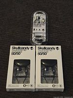 Photo showing two retail boxed Skullcandy Supreme Sound 50/50 earbuds and one Skullcandy Ink'd earbuds in decorative plastic packaging.