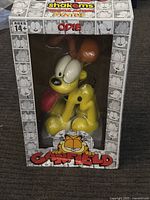 Front view of boxed Odie figure showing figure inside clear window, with Garfield logo and ShakeMS branding on box.