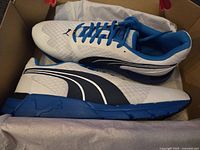 Pair of new Puma sneakers in white, blue, and black inside original box with tissue paper.