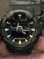 Close-up photo of the black Casio G-Shock men's watch showing analog and digital display and bezel with brand markings.