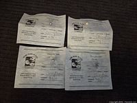 Four loose pearls each attached to a transparent backing with Kobe Pearl & Gem Company paper certificates indicating pearl colors and estimated values lying on a black fabric surface.