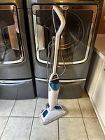 Full view of the BISSELL PowerFresh steam mop standing on tile floor in front of washer and dryer units.