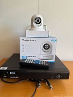 Flir 4K Ultra MPX security hub with Amcrest Wi-Fi Pan/Tilt camera and remote control on top, showing front and some connectors.