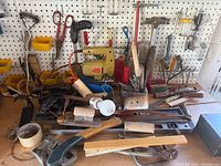 Overview of assorted vintage tools arranged against a pegboard including saws, hammers, drills, scissors, clamps, and small hand tools.