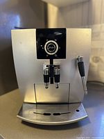 Front view of silver machine showing dual coffee spouts, drip tray and steam wand