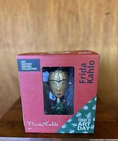 Front view of the boxed Frida Kahlo action figure showing the figure through transparent window and box graphics.