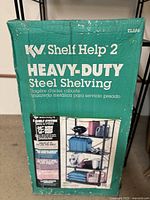 Photo of the green packaging box for the KV Shelf Help 2 Heavy Duty Steel Shelving showing product branding, dimensions, and an illustration of the shelving unit in use.