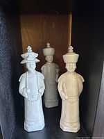 Photo showing three white porcelain Chinese emperor figurines lined up, each wearing traditional headdresses and beaded necklaces.