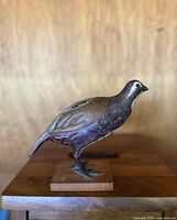 Front and side view of the hand carved wooden quail figurine showing detailed feather pattern and paint on a wooden base.