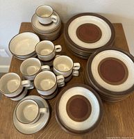 Full set of Denby Potters Wheel plates, cups, saucers and bowls displayed on wooden surface, arranged by type.